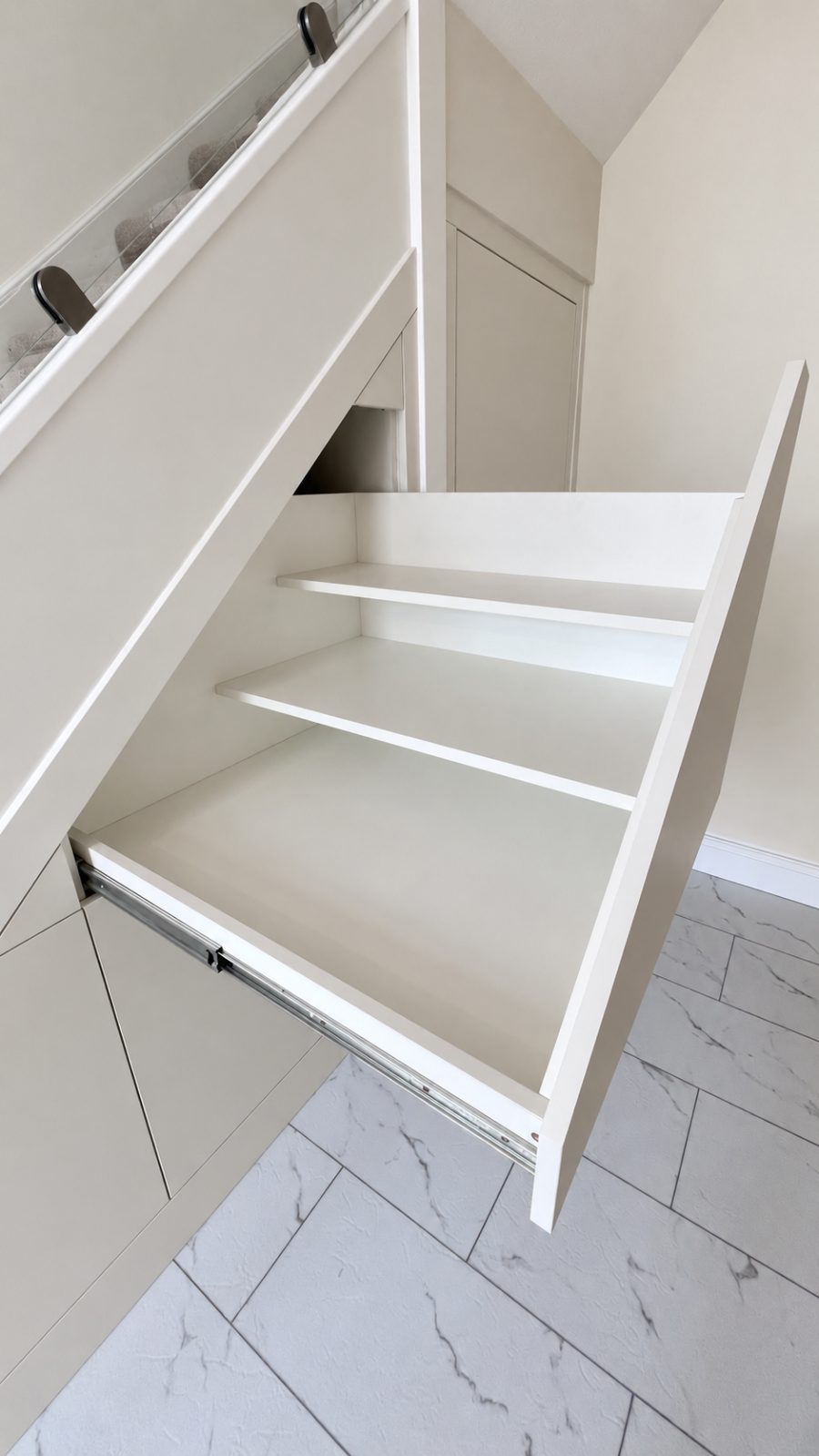 An angled top drawer pulled out under the slope of the stairs, with two shelves inside following the angle